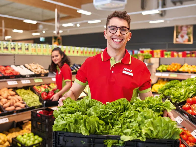 Eine Mitarbeiterin und ein Mitarbeiter tragen Obst und Gemüse Körbe im Markt