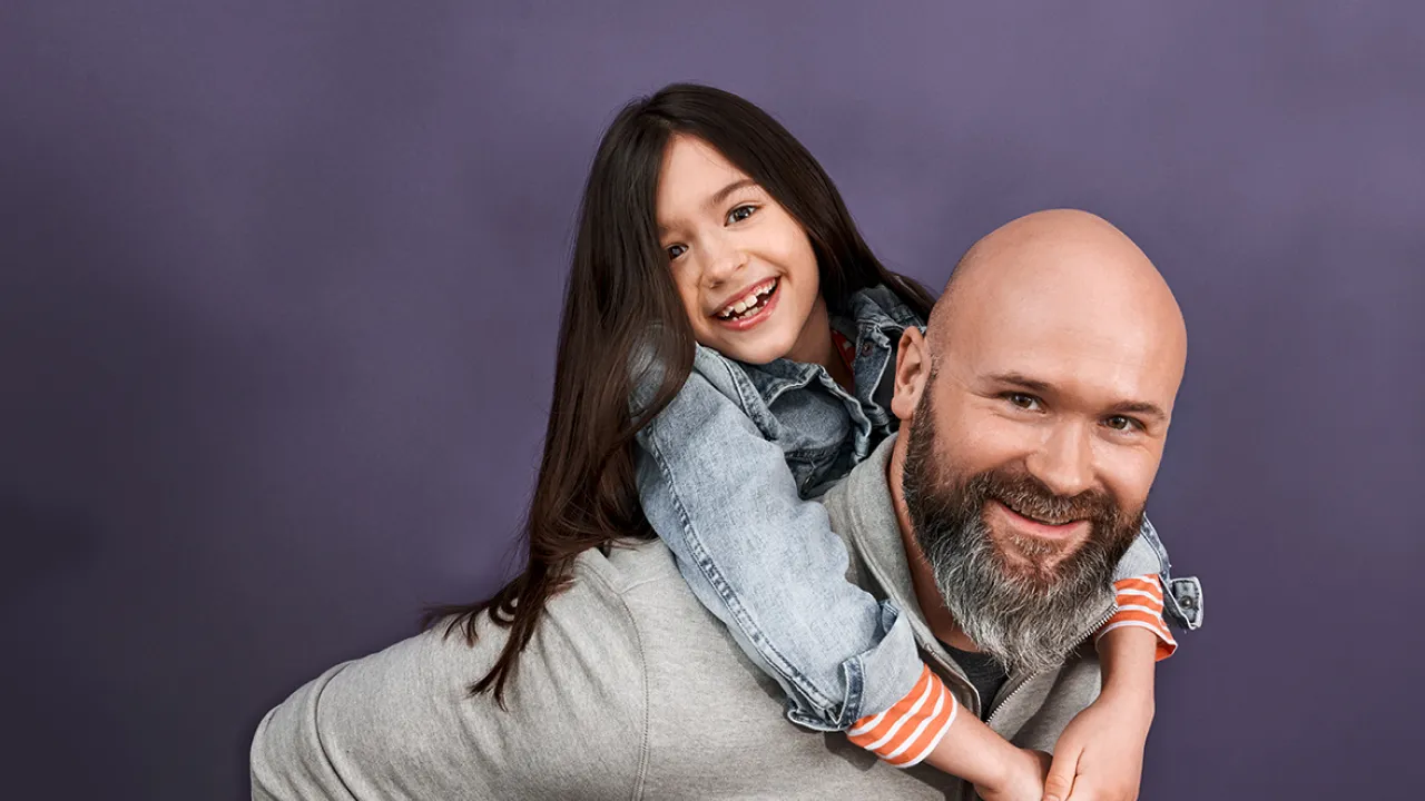 Ein Vater mit seiner Tochter auf dem Rücken vor einem violetten Hintergrund